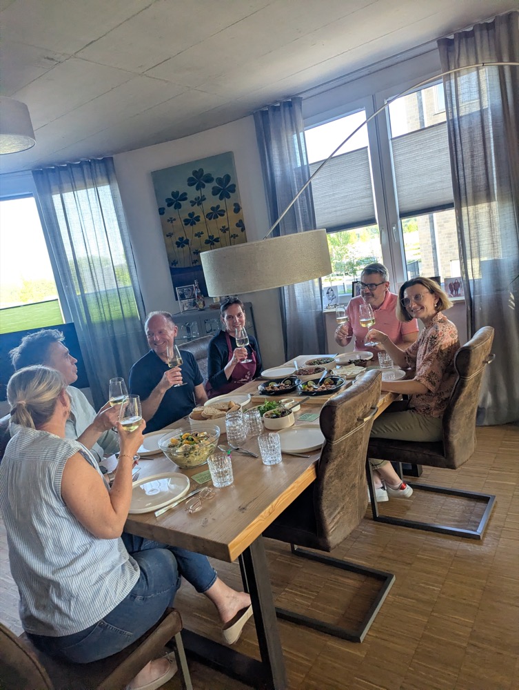 Teilnehmer stoßen bei einem Kochkurs zuhause gemeinsam am Tisch an